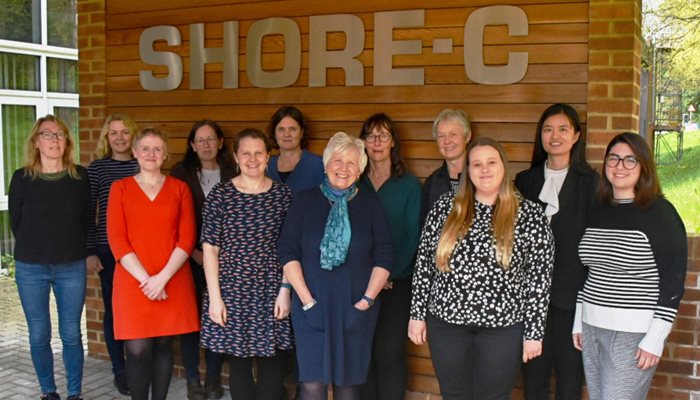 The 12 members of the SHORE-C team pictured together in front of their sign on a brick wall
