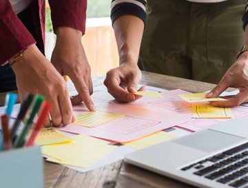 A group of people putting sticky notes on a table with a pen pot and laptop in the foreground