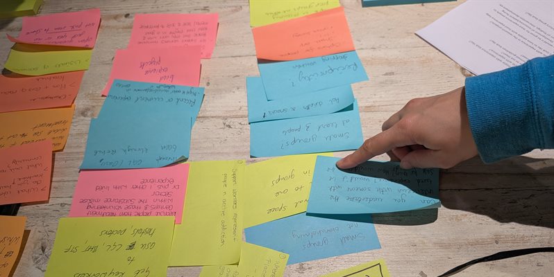 A hand pointing a different coloured post it notes on a table