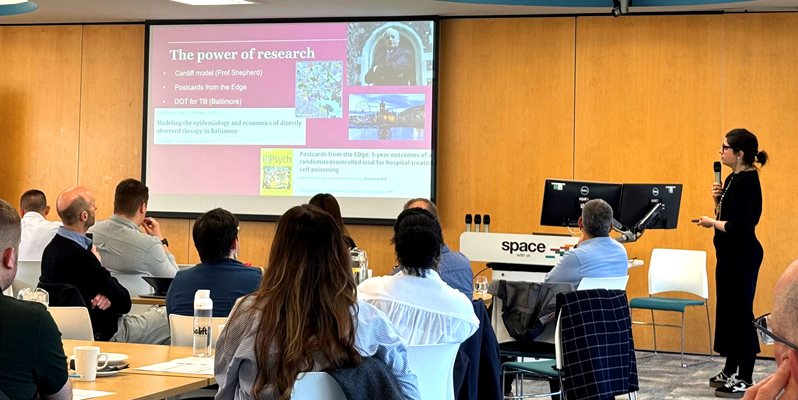 A group of people listening to a presentation in front of a screen with slides and photos on it