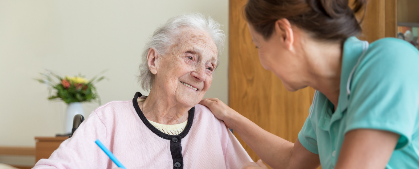 A woman with dementia sat smiling sitting next to her carer