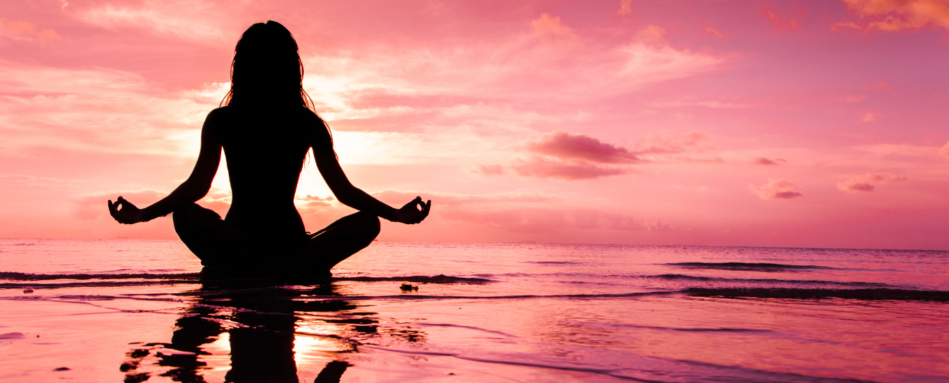 A silhouette sat crossed legged on the beach meditating against a pink background