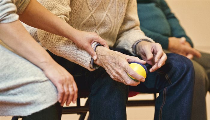 A close up of a carer holding a hand of an elderly person who is holding a ball in one hand