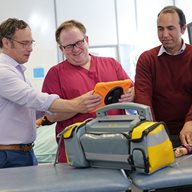 4 people in a hospital with an iPad and simulated dummy on a patient bed