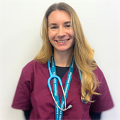 Harri Lewis-Henery, PA Alumna, wearing her scrubs and standing and smiling at the camera