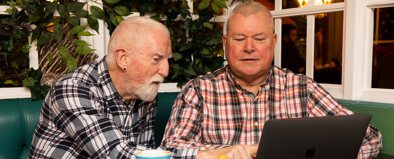 Two men looking at a laptop and drinking tea