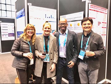 Four HIV researchers wearing lanyards and stood next to posters at a conference