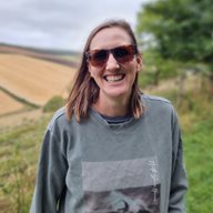 Caroline Ackley pictured outside next to a field and trees wearing sunglasses