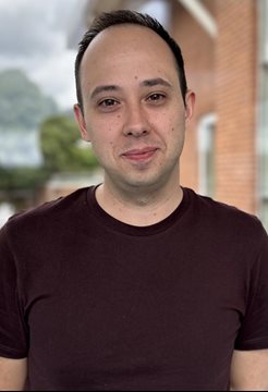 A head and shoulders photo of Dr Fabio Simoes in a purple t shirt next to the medical research building on campus at the BSMS