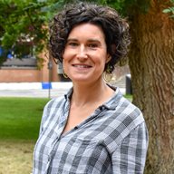 A head and shoulders photo of Maya Semrau, taken outside in front of a green leafy tree