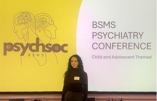 Melis Cobandag stood in front of the board in the lecture theatre with a presentation in the background reading 'BSMS Psychiatry Conference'